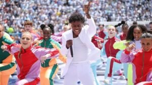 100-224800-fifa-world-cup-final-2026-ceremony-2 - عروبة الاخباري | Oroba News A performer in a white suit sings into a microphone while colorful dancers in vibrant outfits dance around on a stadium stage.