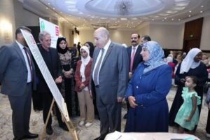 Group of formally dressed people gathered around a poster on an easel at a ceremony in a hotel ballroom.