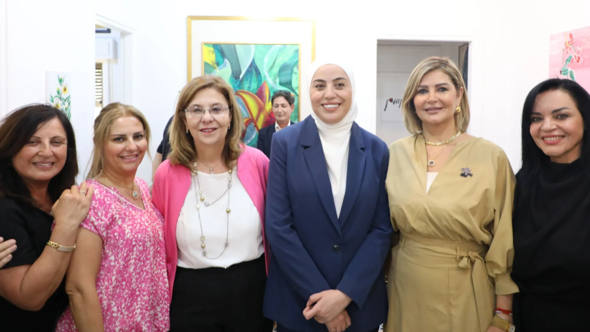 1d6ce568-9eb9-40ee-b08c-12b494538c05 Group of six women smiling at camera in an art gallery, wearing colorful outfits and a blue blazer in the center.
