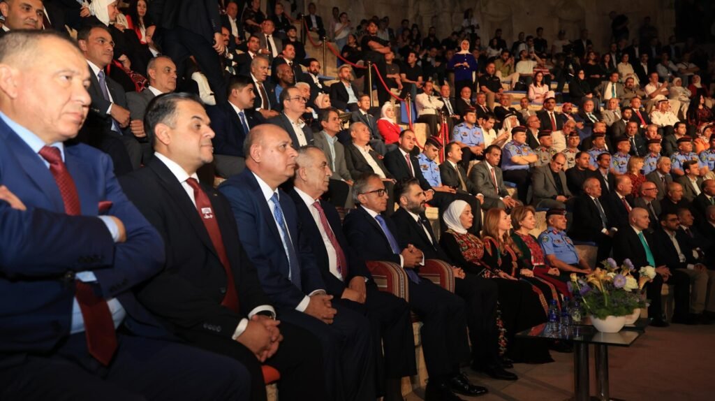 Audience seated in a formal event venue, many in suits and uniforms, paying attention to a ceremony.