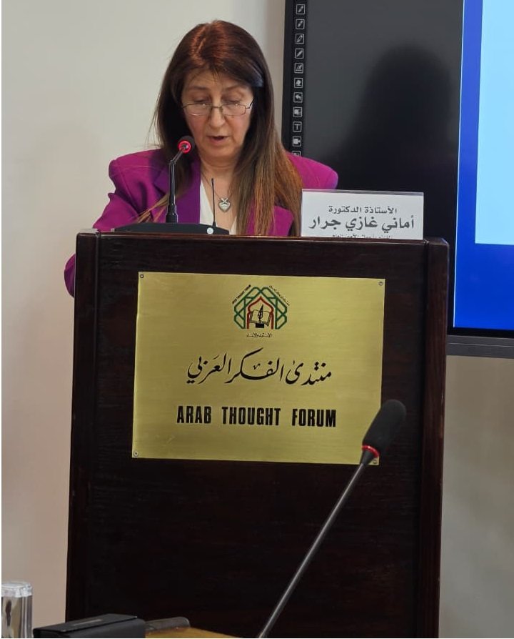 356422_4_1784174984 - عروبة الاخباري | Oroba News Woman in a magenta blazer speaks at a podium labeled Arab Thought Forum; microphone in front.