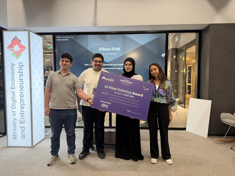 Four people stand together at an event, holding a large purple certificate reading 'In Kind Training Award' with a ministry banner in the background.
