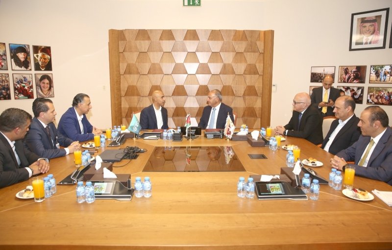 6a4e39dfa8156 - عروبة الاخباري | Oroba News Group of men in suits sit around a large wooden conference table with flags at center, discussing; wall behind features geometric wooden panel and framed photos.