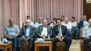 Group of men seated in a formal meeting room, front row in suits listening attentively.