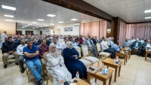Large crowd seated in a conference room, attentively listening to a speaker at the front.