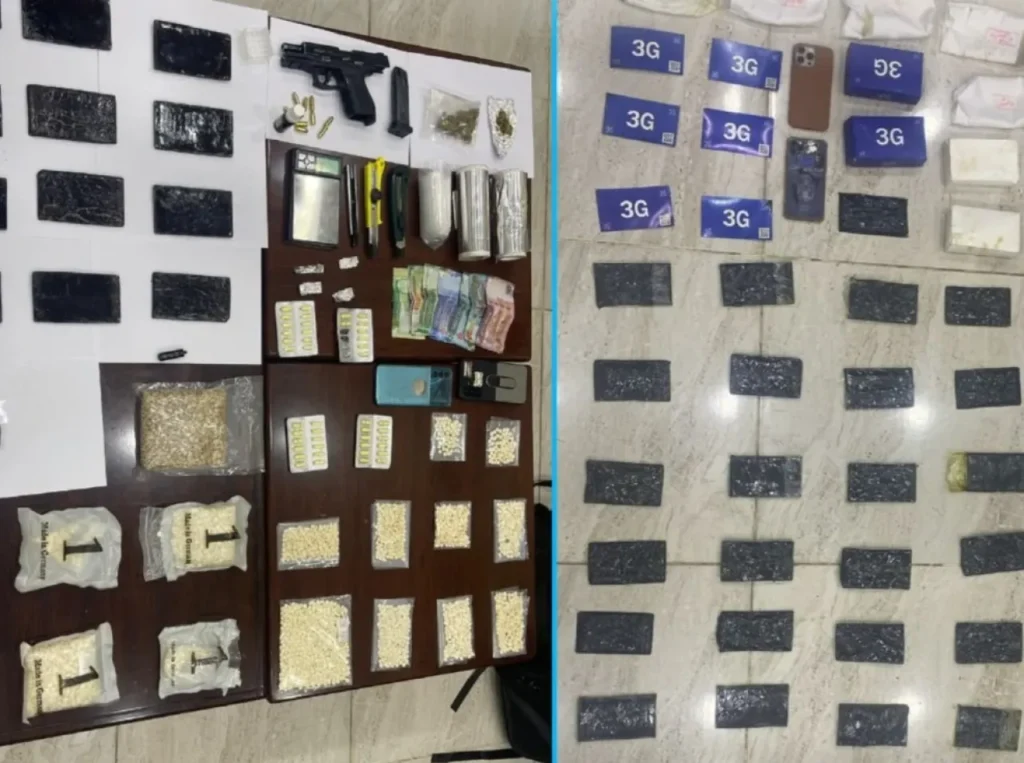 6a5f2fd6a9a77 - عروبة الاخباري | Oroba News Display of seized evidence: handgun with ammo, cash, pills and packets, scales, a mobile phone, and several 3G SIM card boxes arranged on a table.