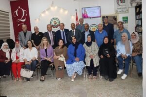 Group of men and women posing for a group photo at a community event in a decorated room with banners and a screen in the background.