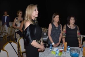 Elegant group of adults standing around a dining table on a nighttime outdoor terrace, dressed in black outfits.