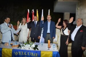 Group of adults standing behind a table at night, raising their hands in a pledge or ceremony with flags in the background.