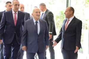 Group of professionally dressed men in suits greeting each other in a bright lobby or hallway edge of a doorway, suggesting a formal meeting or arrival.