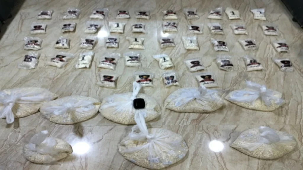 Row of small plastic bags filled with white powder spread on a marble floor, with larger tied bags arranged in front.