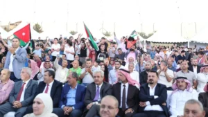 756092 - عروبة الاخباري | Oroba News Large group of people at an outdoor event, some holding Jordanian flags and taking photos with phones.