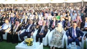 756095 - عروبة الاخباري | Oroba News Large outdoor ceremony with a packed audience under white tents; front row includes officials in suits and a woman in traditional dress.