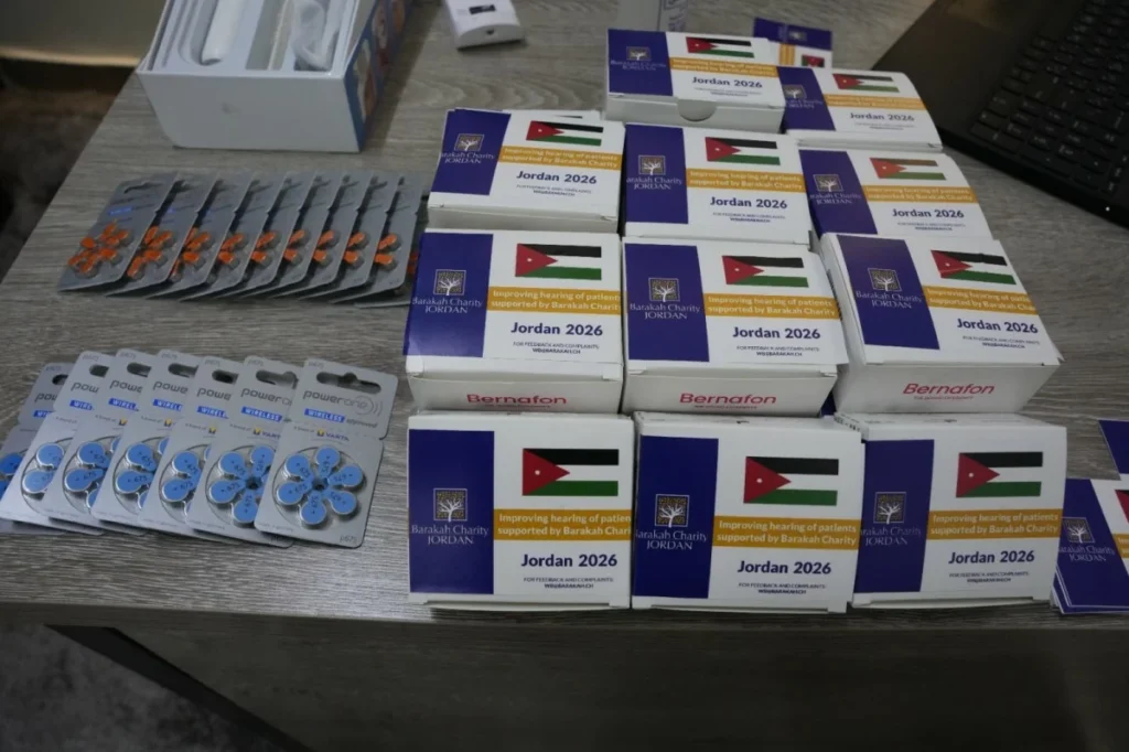 756473 - عروبة الاخباري | Oroba News Boxes labeled Jordan 2026 from Barakah Charity Jordan on a table with Jordan flag graphics, plus blister packs of pills nearby.