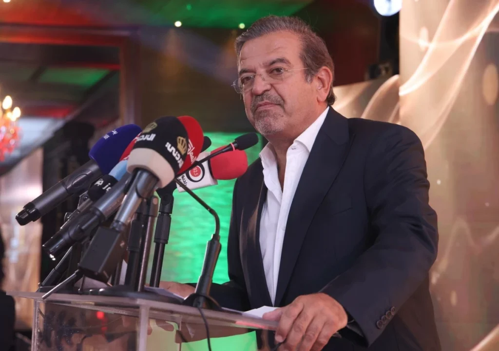 756669 - عروبة الاخباري | Oroba News Man in a dark suit speaking at a podium amid multiple microphones during a press conference, reporters absent in frame.