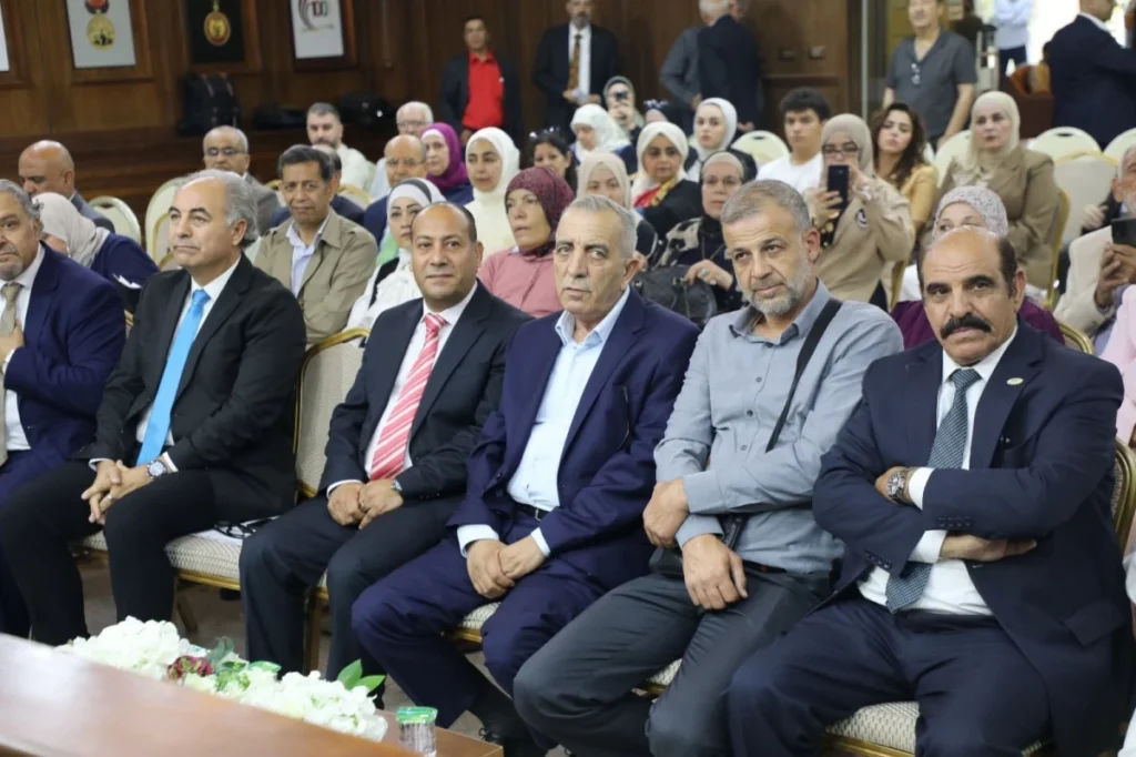 757358 - عروبة الاخباري | Oroba News Front-row group of formally dressed men sitting at a conference, with a diverse audience in the background.