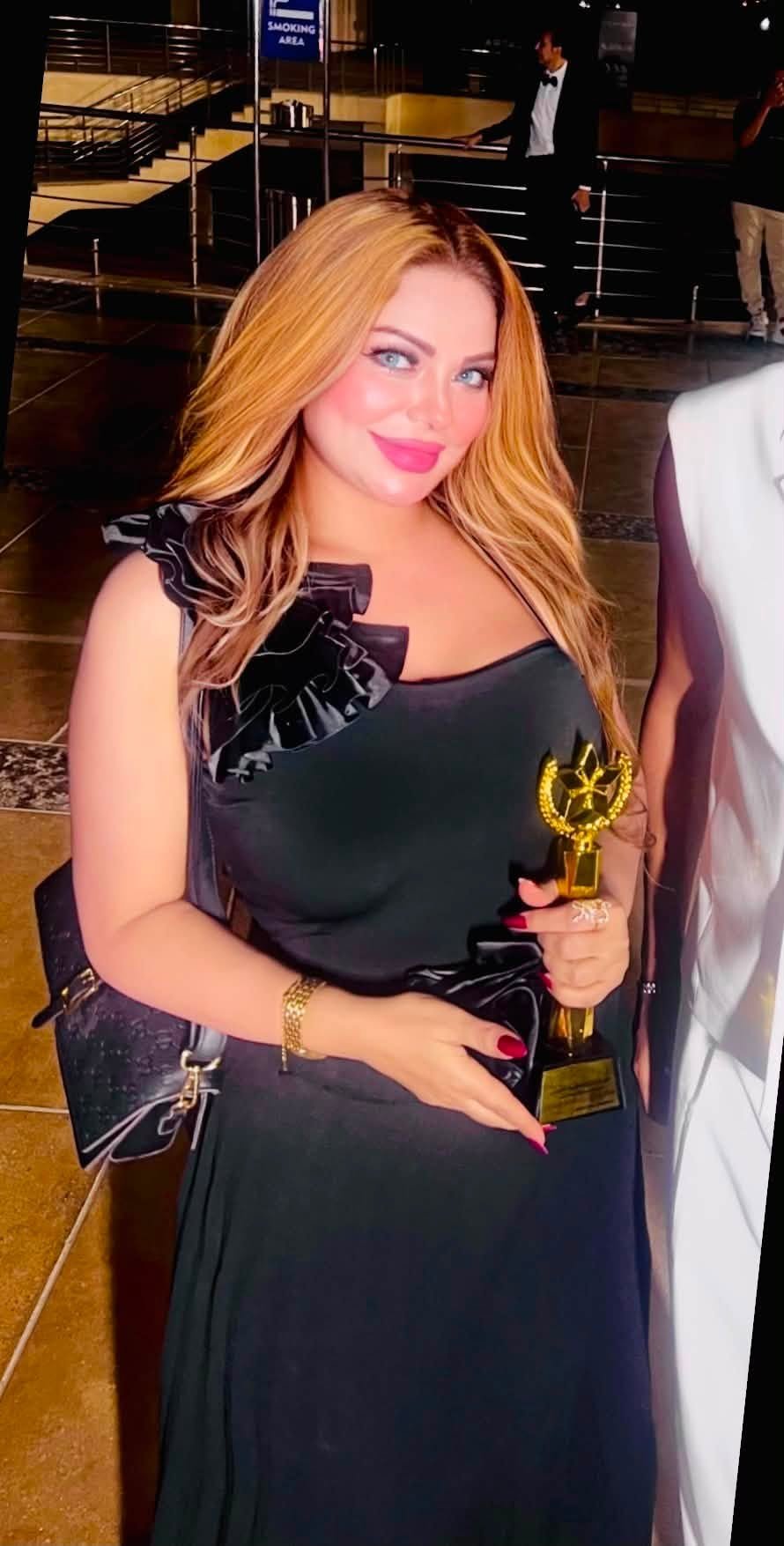 757863535_10243304403807775_675659997874905770_n Woman in a black gown holding a gold trophy at a formal event, smiling for the camera.