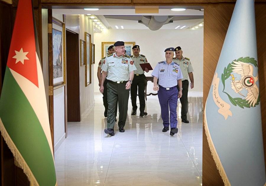 Group of military officers walking down a polished hallway flanked by flags.