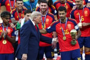 FBL-WC-2026-MATCH104-ESP-ARG-FINAL-TROPHY - عروبة الاخباري | Oroba News Group of men in red striped soccer uniforms wearing medals, posing with a gold trophy while a suited official shakes hands with the captain.