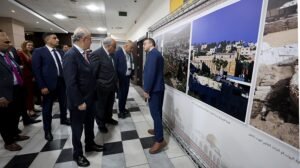 A group of formally dressed people viewing a wall of large city photographs in a hallway exhibition.