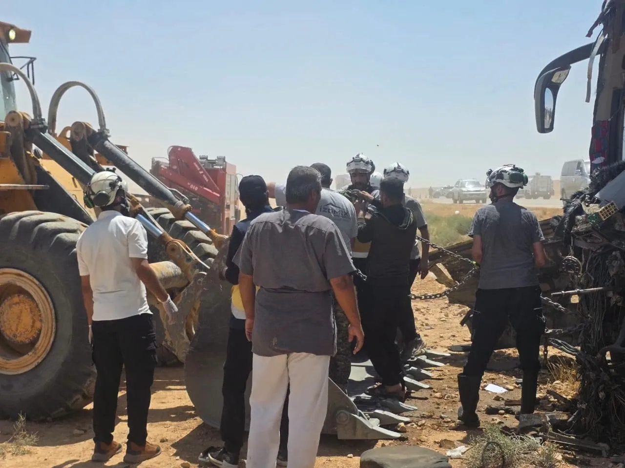 Image1_7202625141458570913050 Rescue crew and bystanders work at a desert crash site with a large excavator lifting debris around a mangled vehicle.
