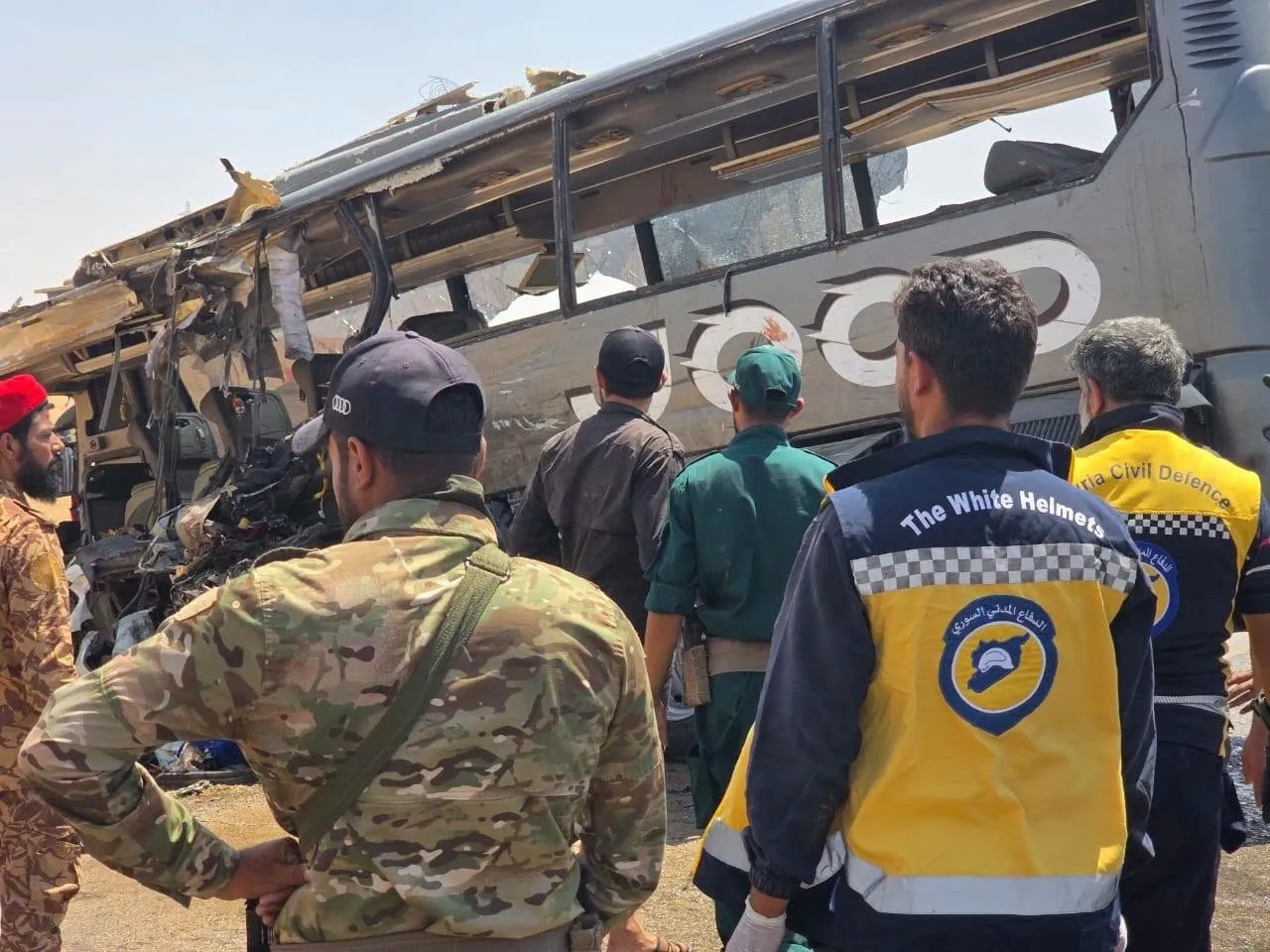 Image2_7202625141458570913050 Rescue workers inspect a damaged bus with a shattered window and debris, standing amidst uniformed personnel at the scene of a crash.