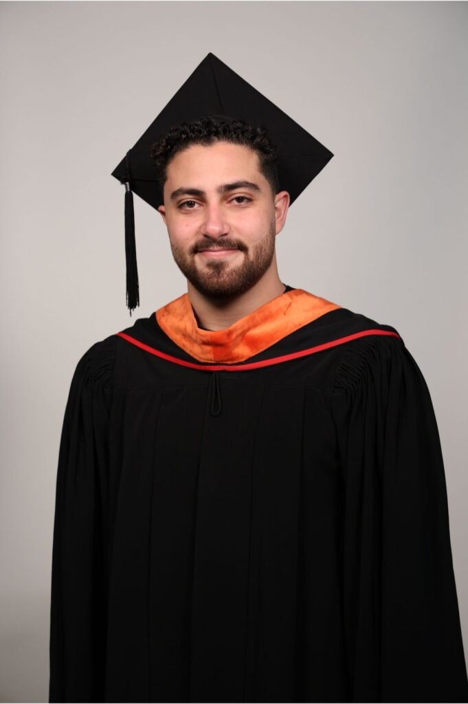 Graduate in a black cap and gown with an orange hood, smiling at the camera.