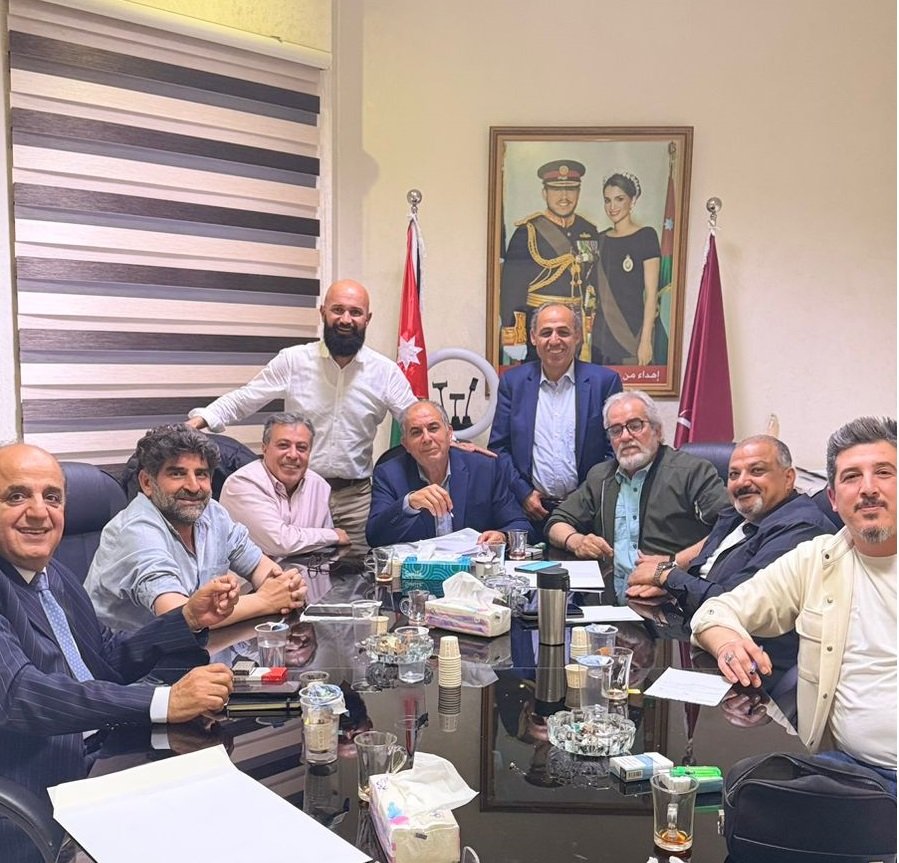 WhatsApp Image 2026-07-07 at 111906 AM - عروبة الاخباري | Oroba News Group of men in a formal meeting around a glass conference table in an office, with flags and a framed portrait in the background.