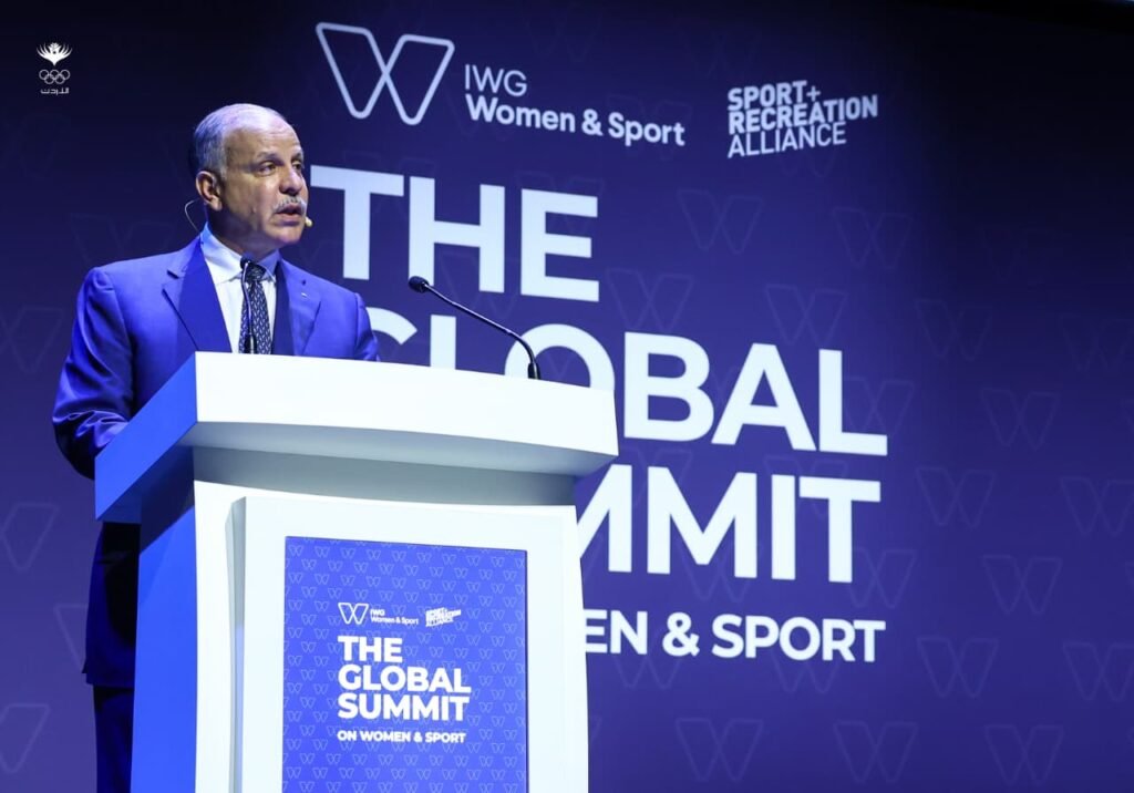 WhatsApp Image 2026-07-10 at 32414 PM - عروبة الاخباري | Oroba News Male presenter in a blue suit speaks at a podium on a stage for The Global Summit on Women & Sport.