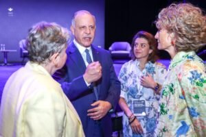 WhatsApp Image 2026-07-10 at 32414 PM1 - عروبة الاخباري | Oroba News Group of four adults in a circle on a stage with purple lighting; man in a blue suit gesturing as three others listen.