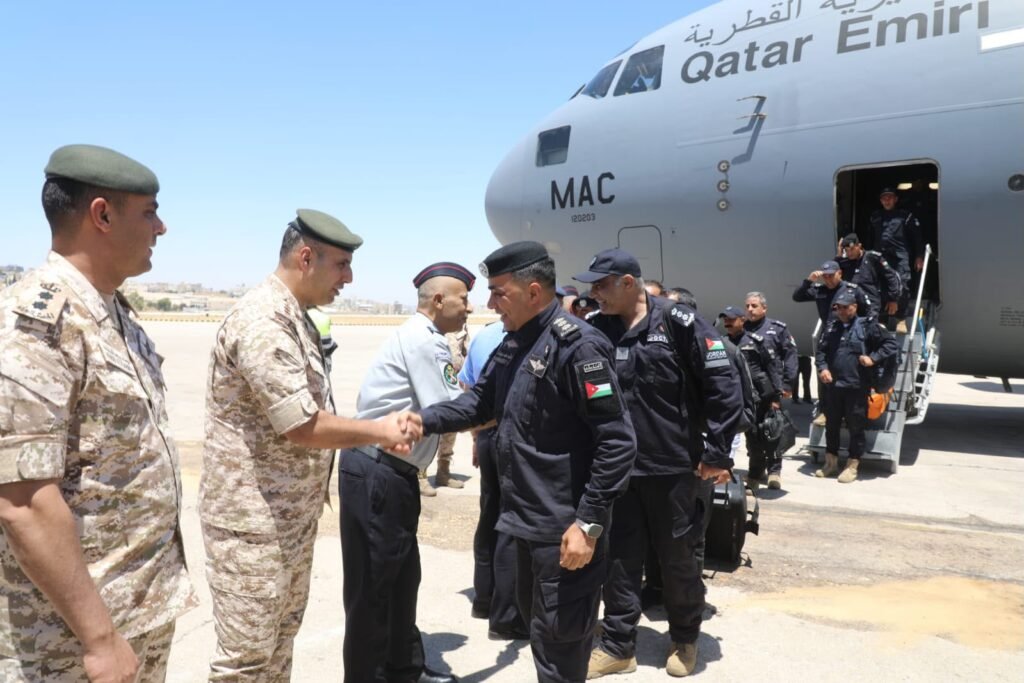 Military officers in uniform shake hands on a sunlit tarmac beside a large Qatar Emiri aircraft as troops stand in line to board/exit the plane.
