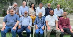 WhatsApp Image 2026-07-15 at 80514 PM1 - عروبة الاخباري | Oroba News Twelve adults posing for a group photo on outdoor steps with greenery in the background.
