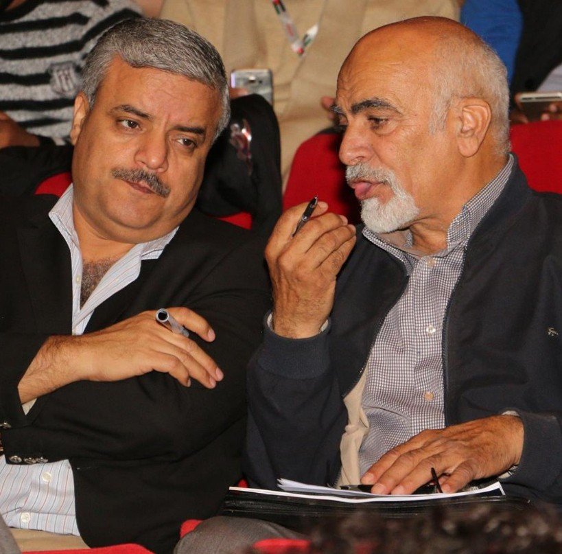 WhatsApp Image 2026-07-15 at 80515 PM - عروبة الاخباري | Oroba News Two men seated closely, one with a pen, discussing papers on a lap in a red‑theater setting.