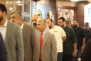 Line of men in smart casual and business attire standing in a hallway, waiting or lining up together indoors.