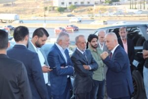Group of men in suits gathered outside a vehicle, engaging in conversation by a black SUV on a roadside.