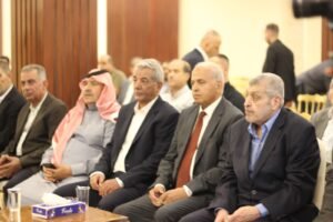 Group of men in suits seated at a formal meeting, one wearing a red-and-white keffiyeh.