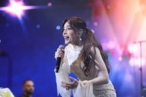 WhatsApp Image 2026-07-17 at 121755 PM4 - عروبة الاخباري | Oroba News Female singer in a white lace dress performs on stage, holding a microphone.