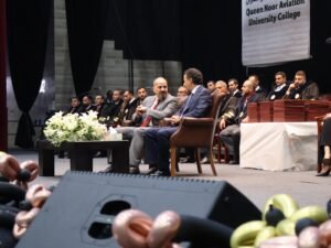 WhatsApp Image 2026-07-18 at 104002 AM 2 - عروبة الاخباري | Oroba News Group of officials seated on a stage during a formal ceremony, with a white flower arrangement on a table in front.