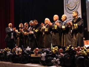 WhatsApp Image 2026-07-18 at 104003 AM 2 - عروبة الاخباري | Oroba News Group of men in academic robes applauding on stage during a ceremony, balloons at the front.