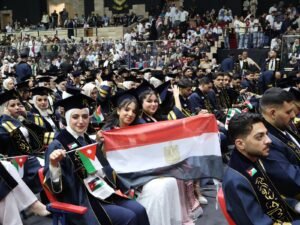 WhatsApp Image 2026-07-18 at 104003 AM - عروبة الاخباري | Oroba News Graduates in navy blue gowns and caps, waving Jordanian and Egyptian flags at a crowded graduation ceremony.