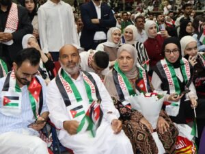 WhatsApp Image 2026-07-18 at 104003 AM 5 - عروبة الاخباري | Oroba News People at a ceremony wearing Jordanian flag sashes, seated in a crowded venue, smiling and posing for photos.