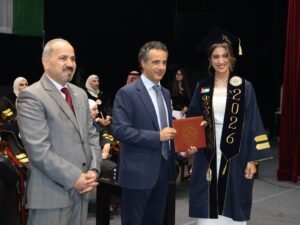 WhatsApp Image 2026-07-18 at 104005 AM 6 - عروبة الاخباري | Oroba News Graduate in a navy cap and gown with a 2026 sash receives a diploma from a suited official at a ceremony, Jordan flag on sash visible.