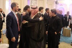 WhatsApp Image 2026-07-18 at 112232 AM 1 - عروبة الاخباري | Oroba News Two men hug at a formal event, one in a black thobe with a red-and-white keffiyeh, surrounded by other suited guests in a ballroom.