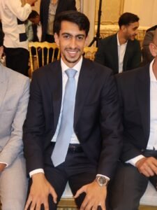 WhatsApp Image 2026-07-18 at 112232 AM 3 - عروبة الاخباري | Oroba News Young man in a navy suit and light blue tie smiles at the camera at a formal event.