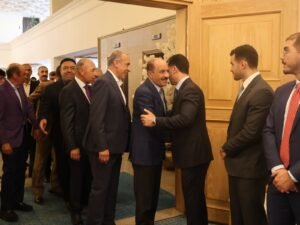 WhatsApp Image 2026-07-18 at 112234 AM 4 - عروبة الاخباري | Oroba News Line of men in suits greet at a doorway; two men shake hands as others wait in a formal indoor setting.