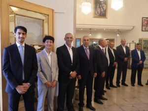 WhatsApp Image 2026-07-18 at 112234 AM 6 - عروبة الاخباري | Oroba News Nine men in suits stand in a row for a formal photograph in a reception area inside a building.