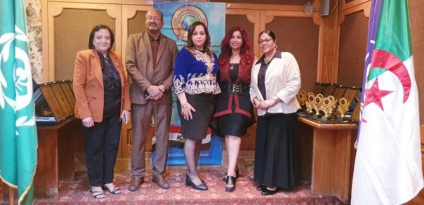 Six adults in business attire posing at an awards ceremony, with trophies on display and flags on either side.