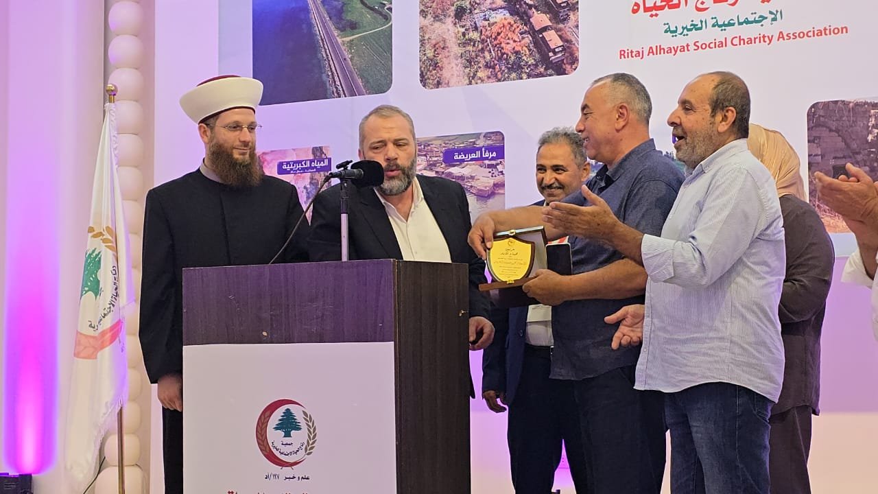 WhatsApp Image 2026-07-22 at 120119 PM 1 Man in a white turban and black outfit speaks at a podium as a group of men present a plaque during a charity event.