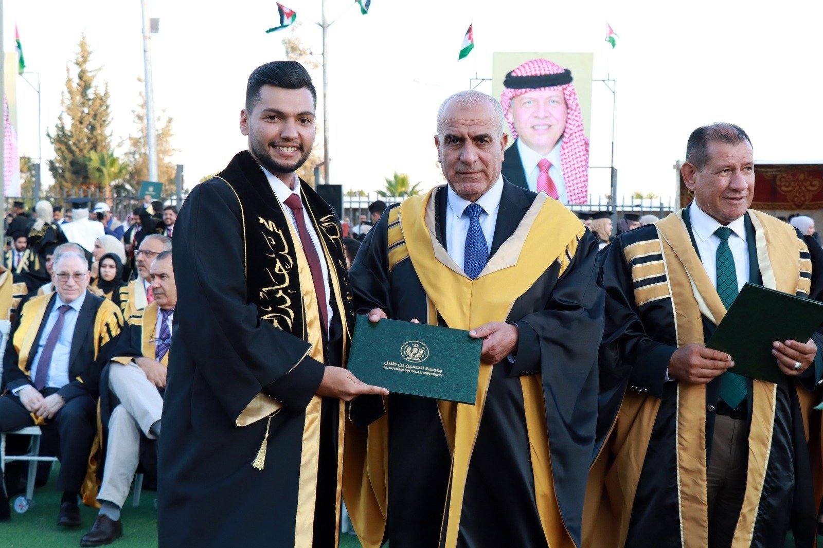 WhatsApp Image 2026-07-23 at 62958 PM1 Graduate in black and gold gown hands a diploma to an older man in ceremonial robes at a graduation ceremony