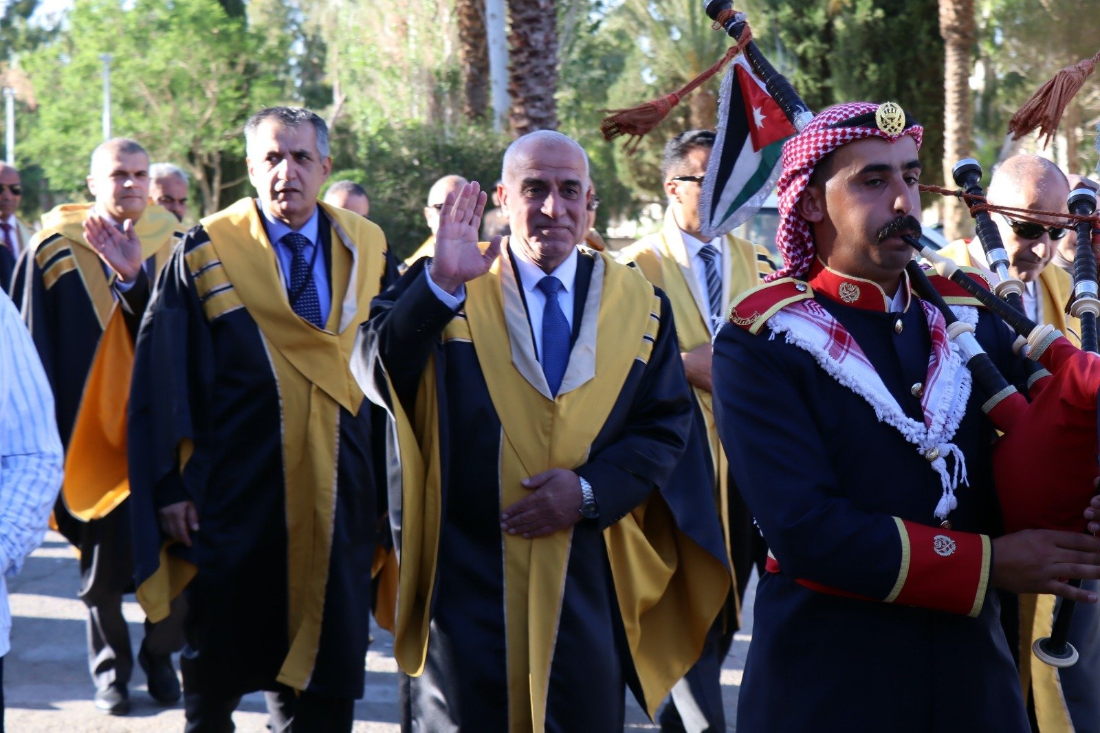 WhatsApp Image 2026-07-23 at 63000 PM1 Group of men in yellow-trimmed ceremonial robes marching in a parade; central man raises his right hand, Jordan flag visible in the background.